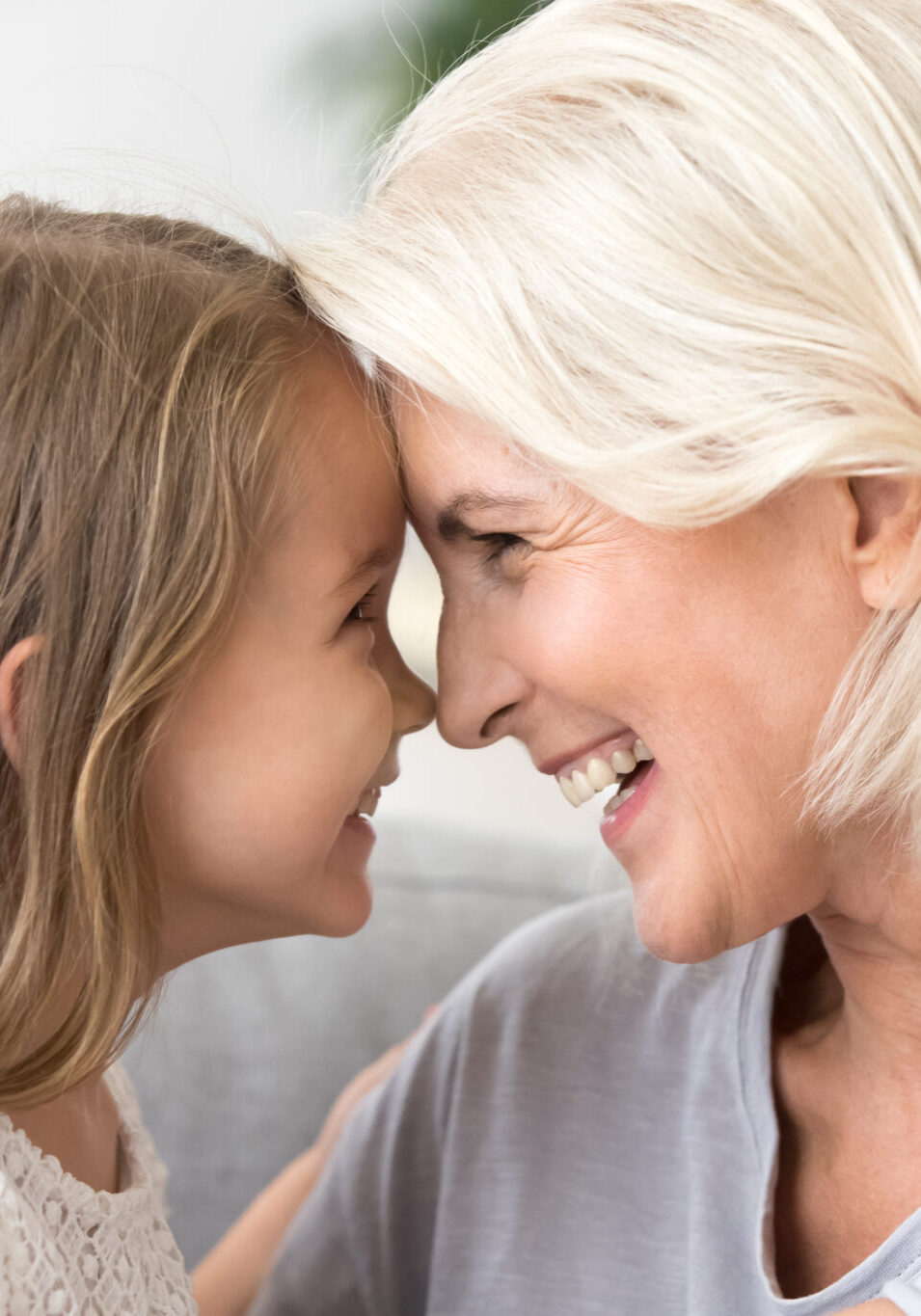 Happy middle-aged mature grandma and little preschool granddaughter touching noses laughing together, smiling loving old grandmother granny and cute carefree grandkid girl having fun playing at home