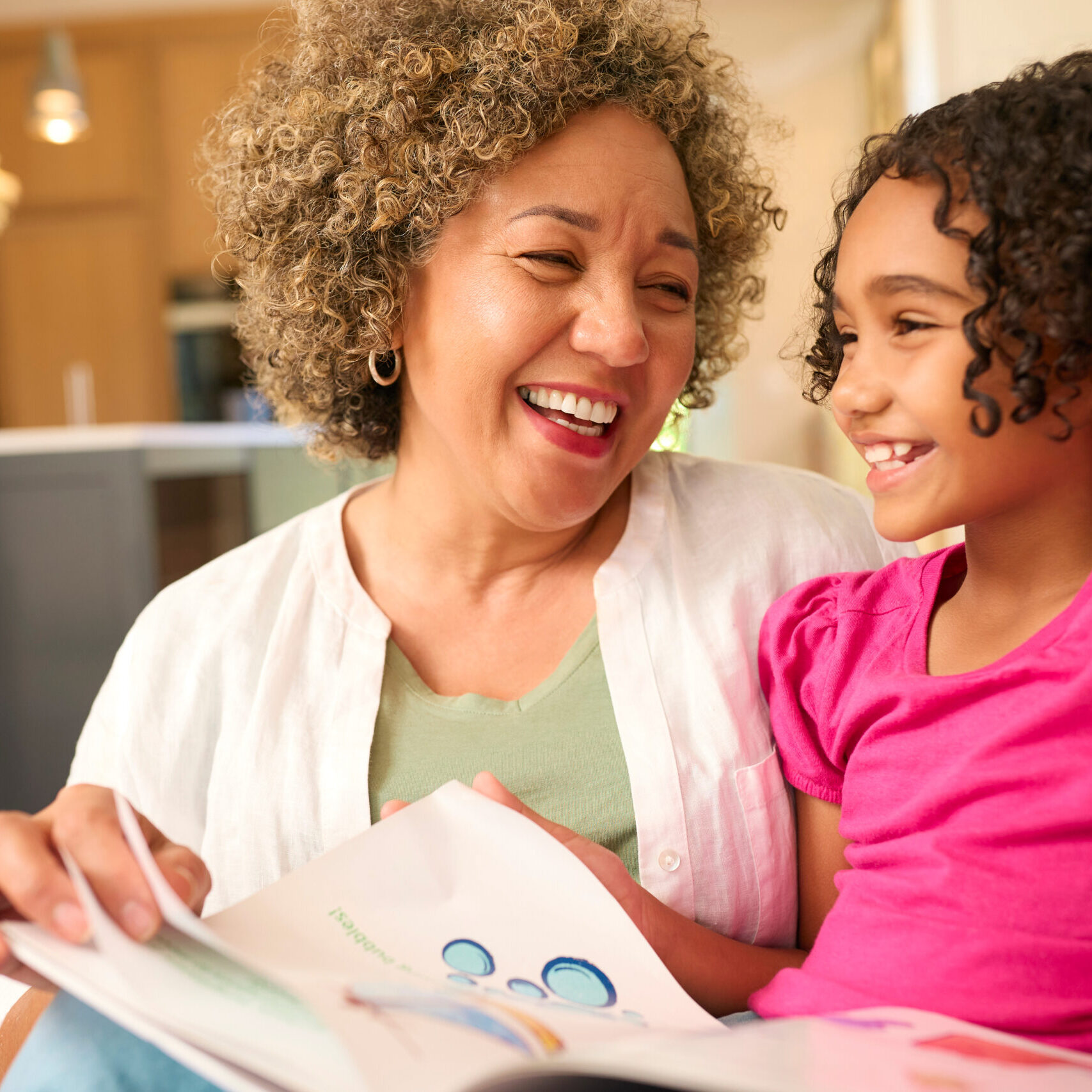 Grandmother Looking After Granddaughter At Home Sitting On Sofa Reading A Story Together